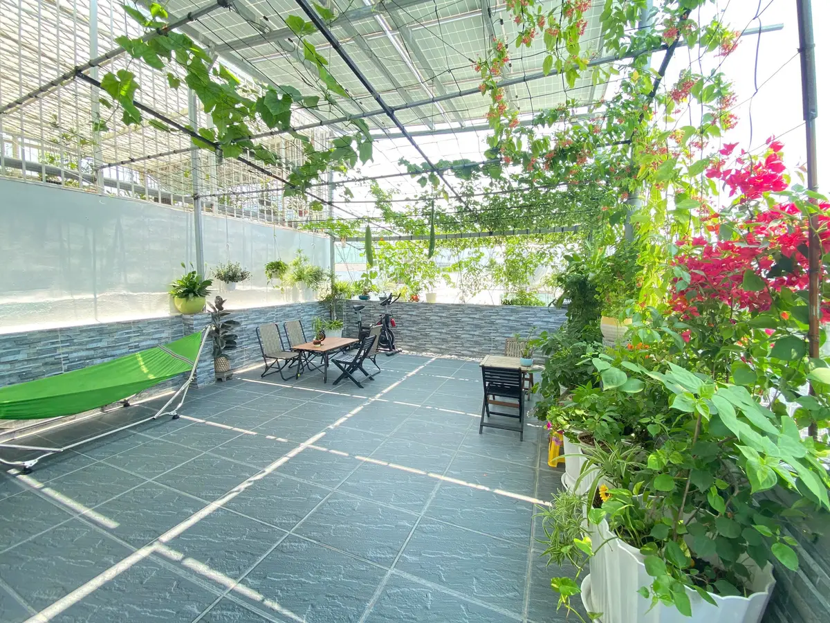 Eine geflieste Dachterrasse unter einem Rankgitter mit Hängematte, kleinem Tisch mit Klappstühlen, Heimtrainer und Bougainvillea in Töpfen.