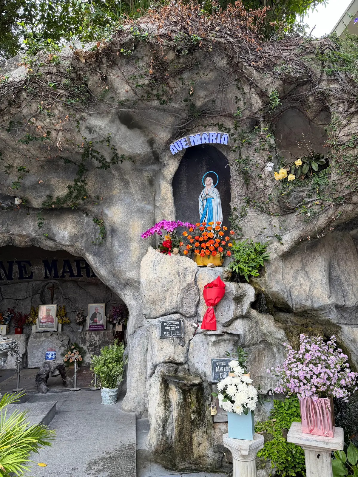 A statue of the Virgin Mary in a rock niche under an Ave Maria sign, with flowers placed below.