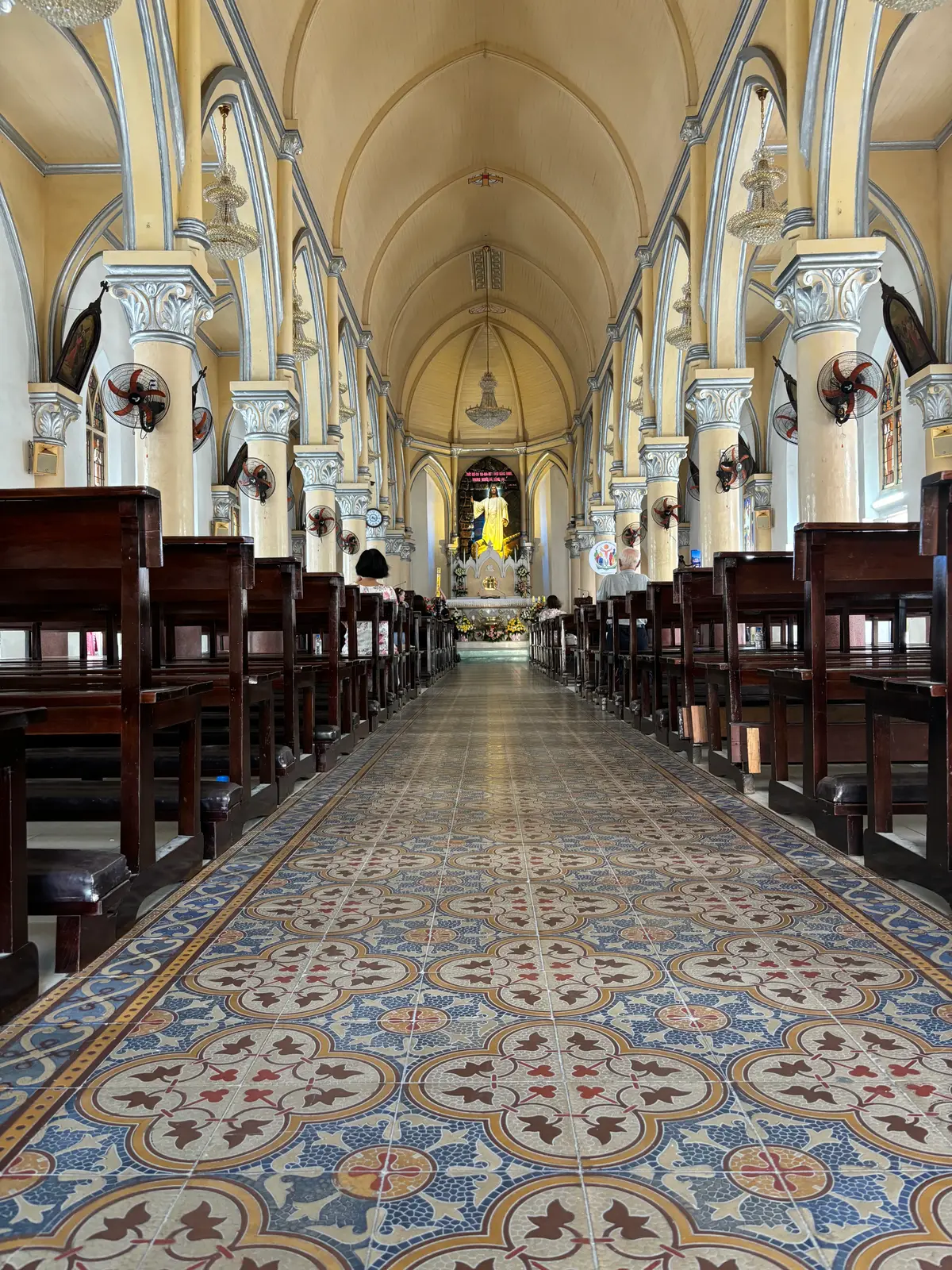 The cathedral interior: rows of dark wooden pews on a patterned tile floor leading to the altar under a vaulted ceiling.