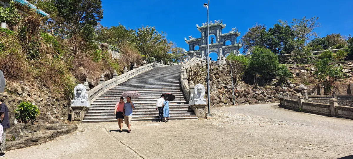 린응사(Linh Ung Pagoda) 문까지 이어지는 넓은 돌계단. 양옆에 돌사자가 있고 계단에 방문객들이 있어요.