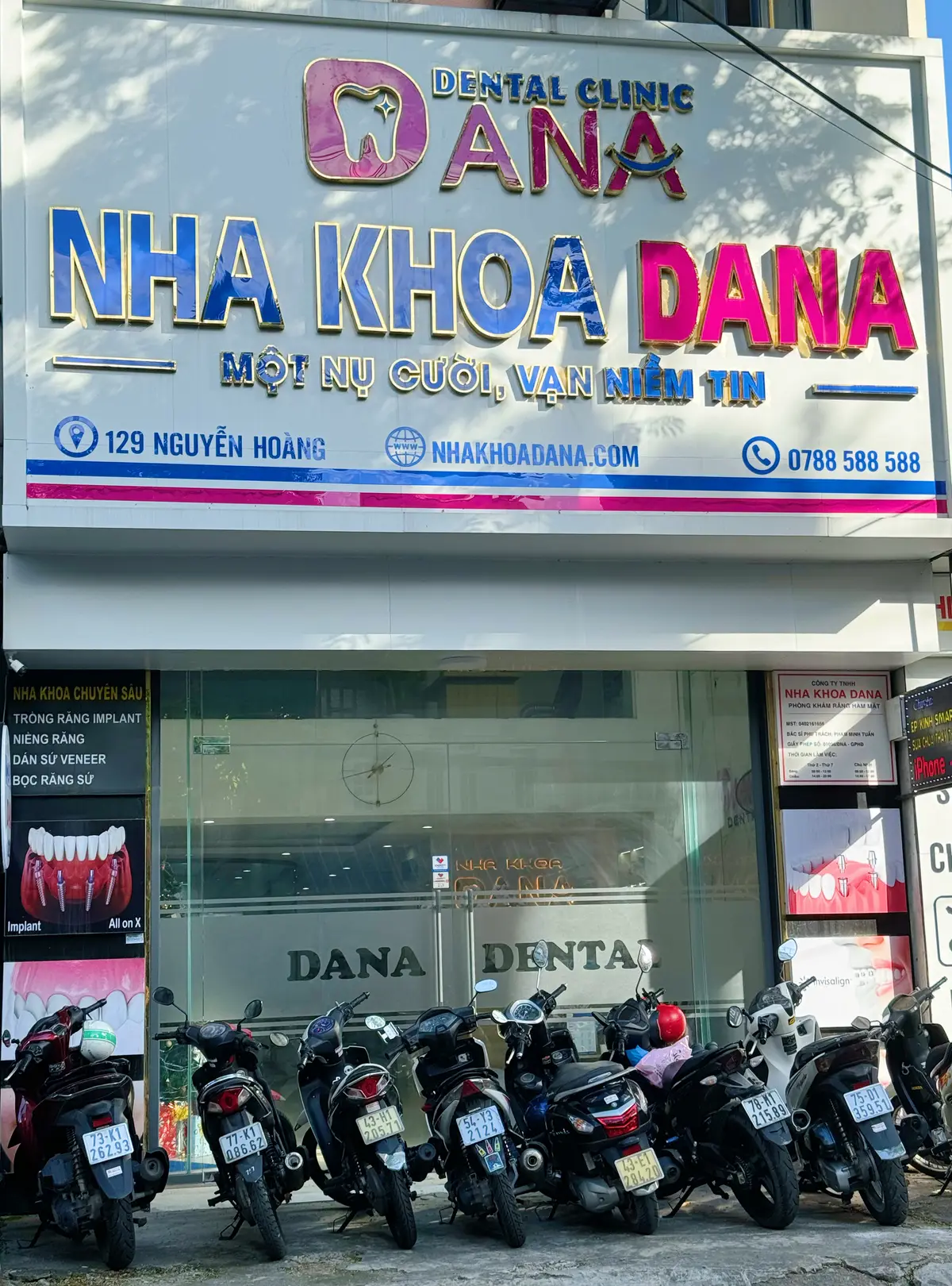 大きな電飾看板とガラスのドアがあり、手前にバイクが並ぶNha Khoa Danaの店頭。