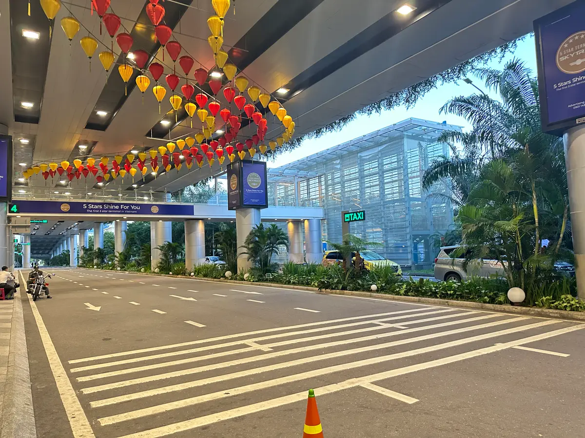 航站楼旁一条有顶的空车道，有斑马线，背景有绿色“TAXI”标牌，天花板上挂着灯笼。