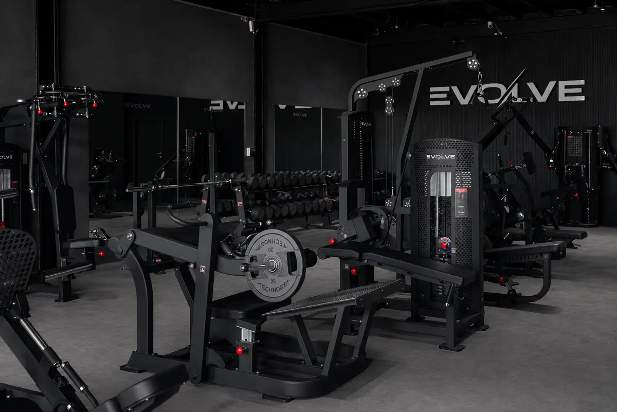 Weight machines and cable stations in a dark, modern gym with the Evolve logo overhead