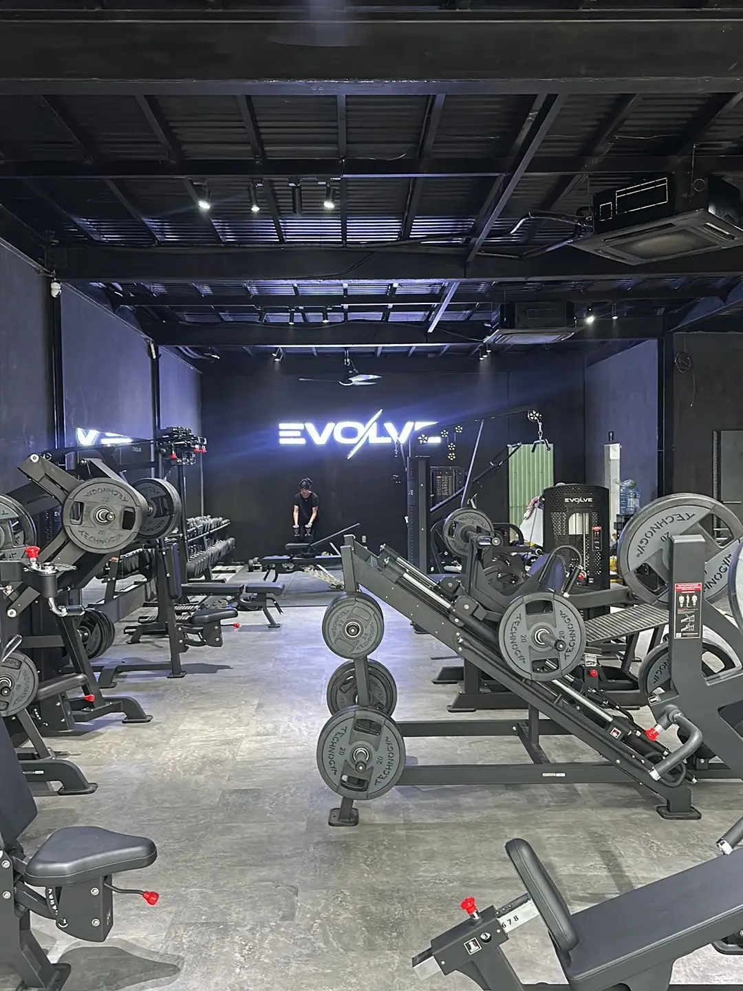 Gym floor with plate-loaded machines and a lit Evolve sign on the back wall