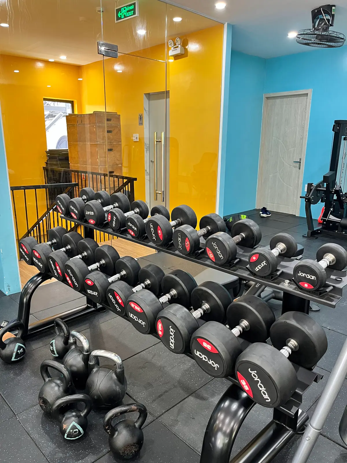 Rack of black dumbbells in a gym with yellow walls