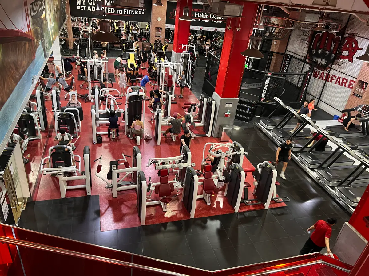 Large red-themed gym floor seen from above, with rows of weight machines