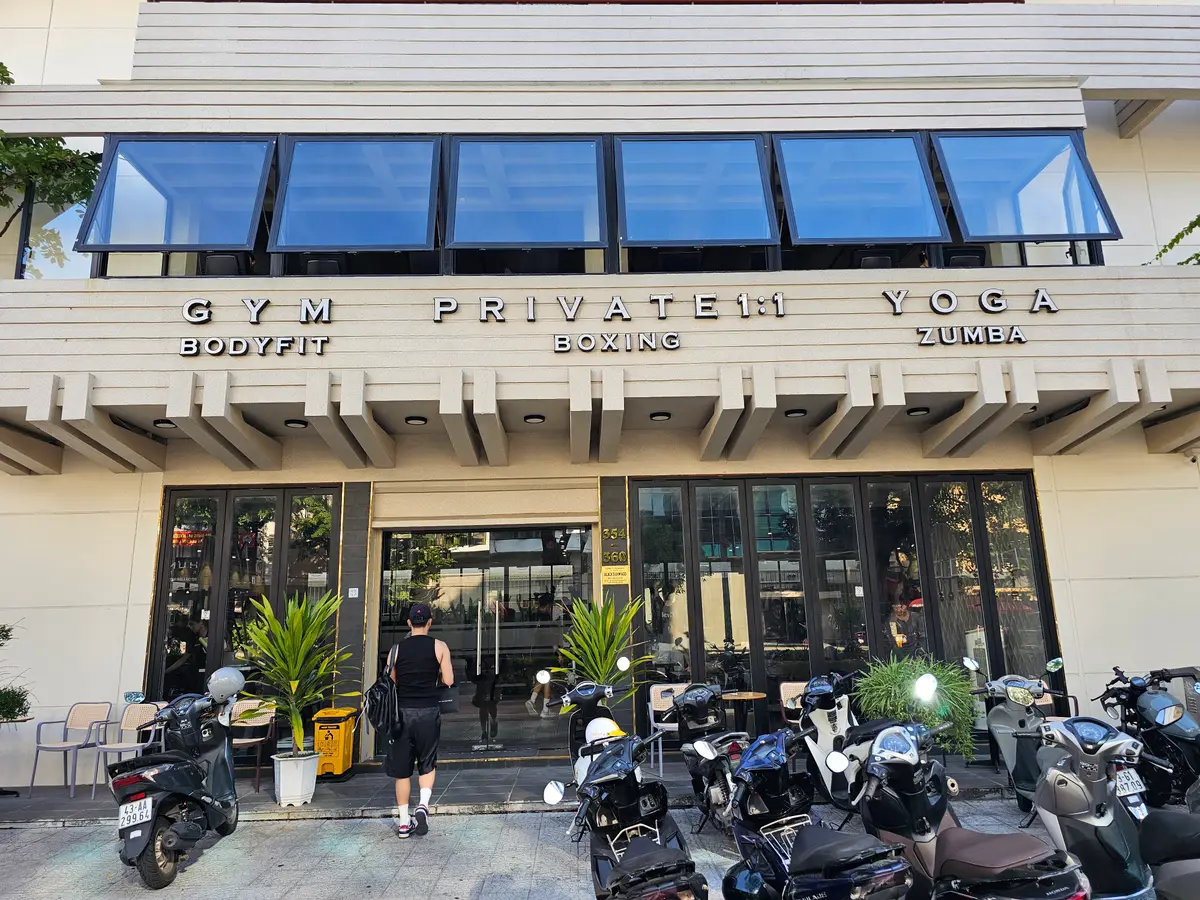 Modern multi-storey building with a gym sign above glass windows and scooters parked out front