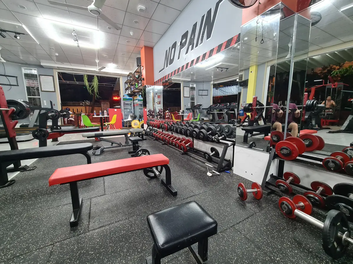 Gym floor with benches, dumbbells and red-framed machines under bright lights