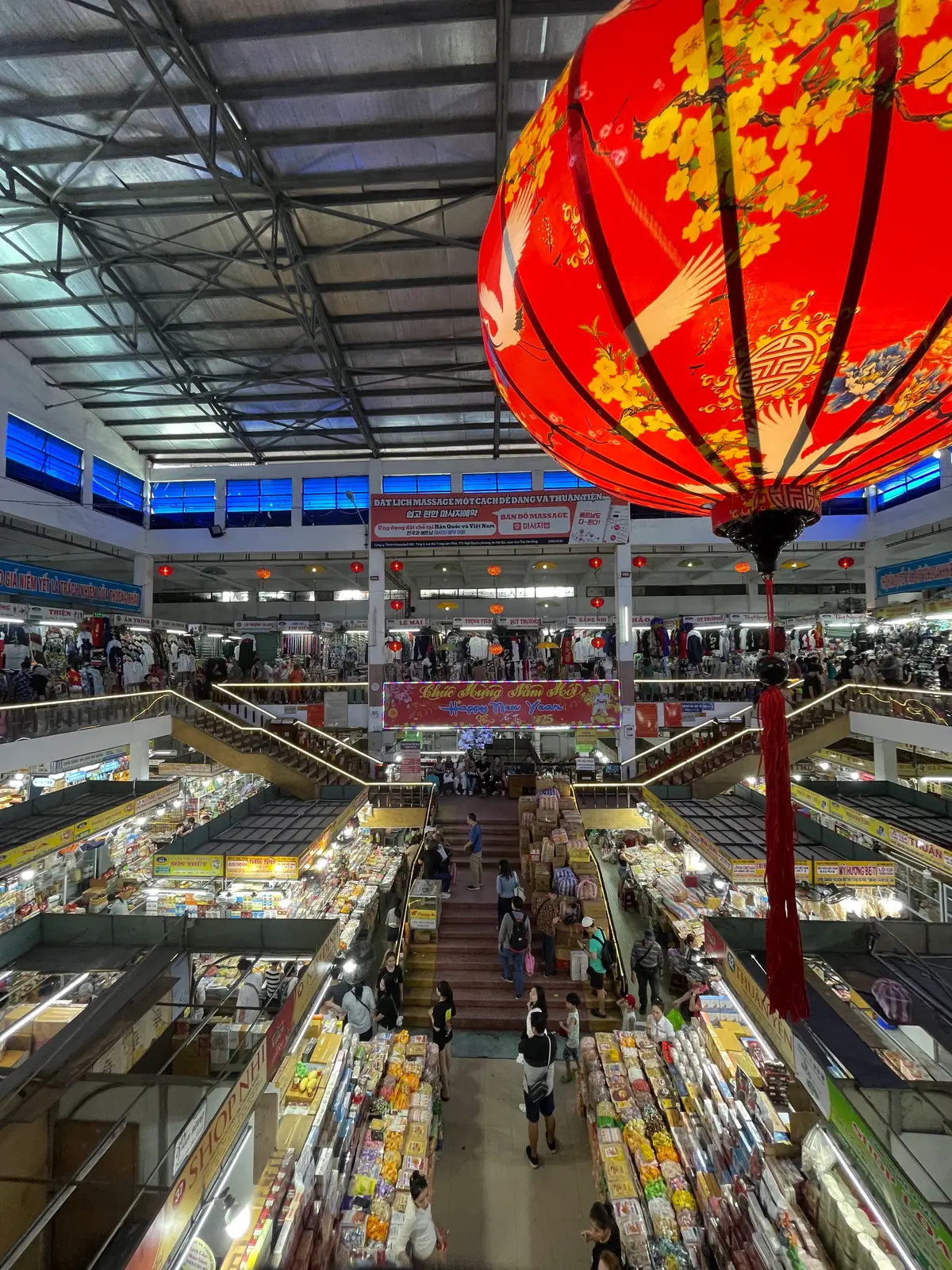 A large red lantern hanging over the market's central hall, with rows of stalls below and a gallery of shops above.