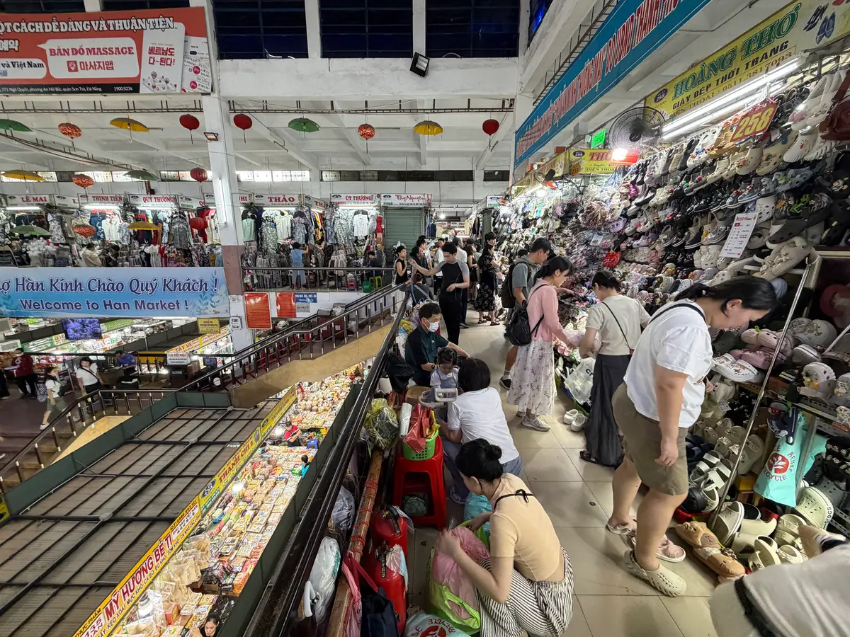 A narrow aisle between clothing and souvenir stalls, with shoppers browsing.