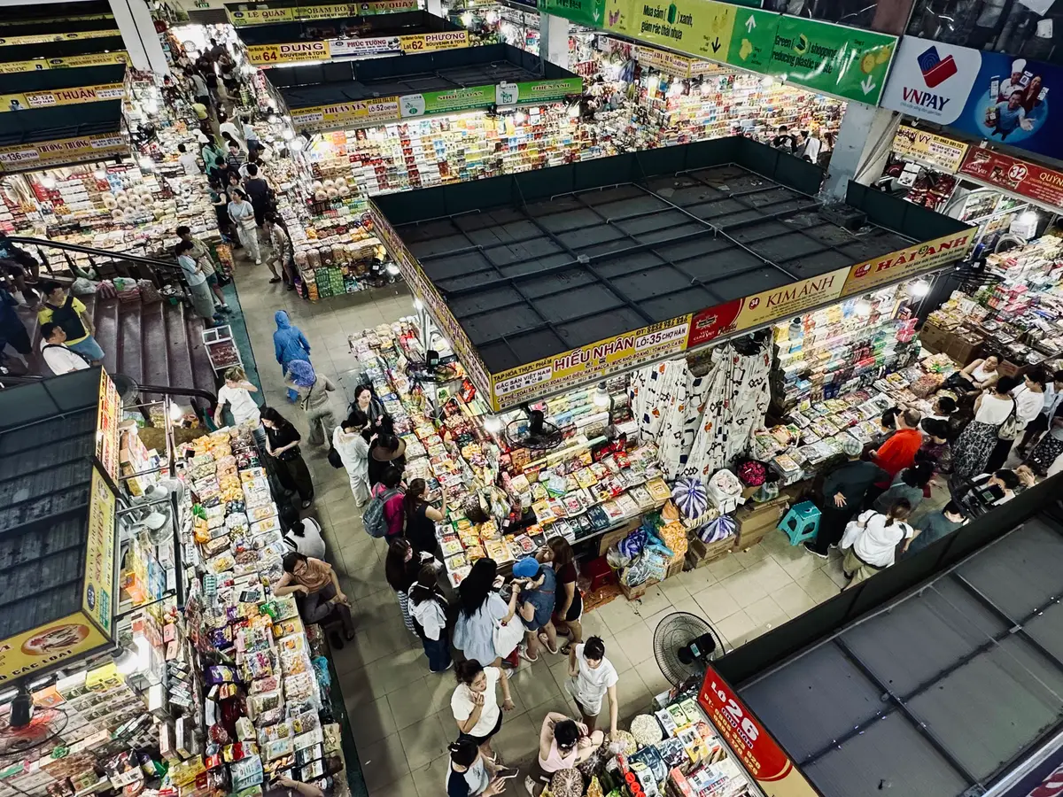 Looking down from the upper floor onto tightly packed stalls and shoppers walking between them.