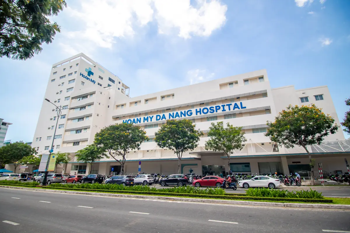 가로수가 늘어선 거리 위로 파란 글씨로 이름이 적힌 흰색 Hoan My Da Nang Hospital 건물.