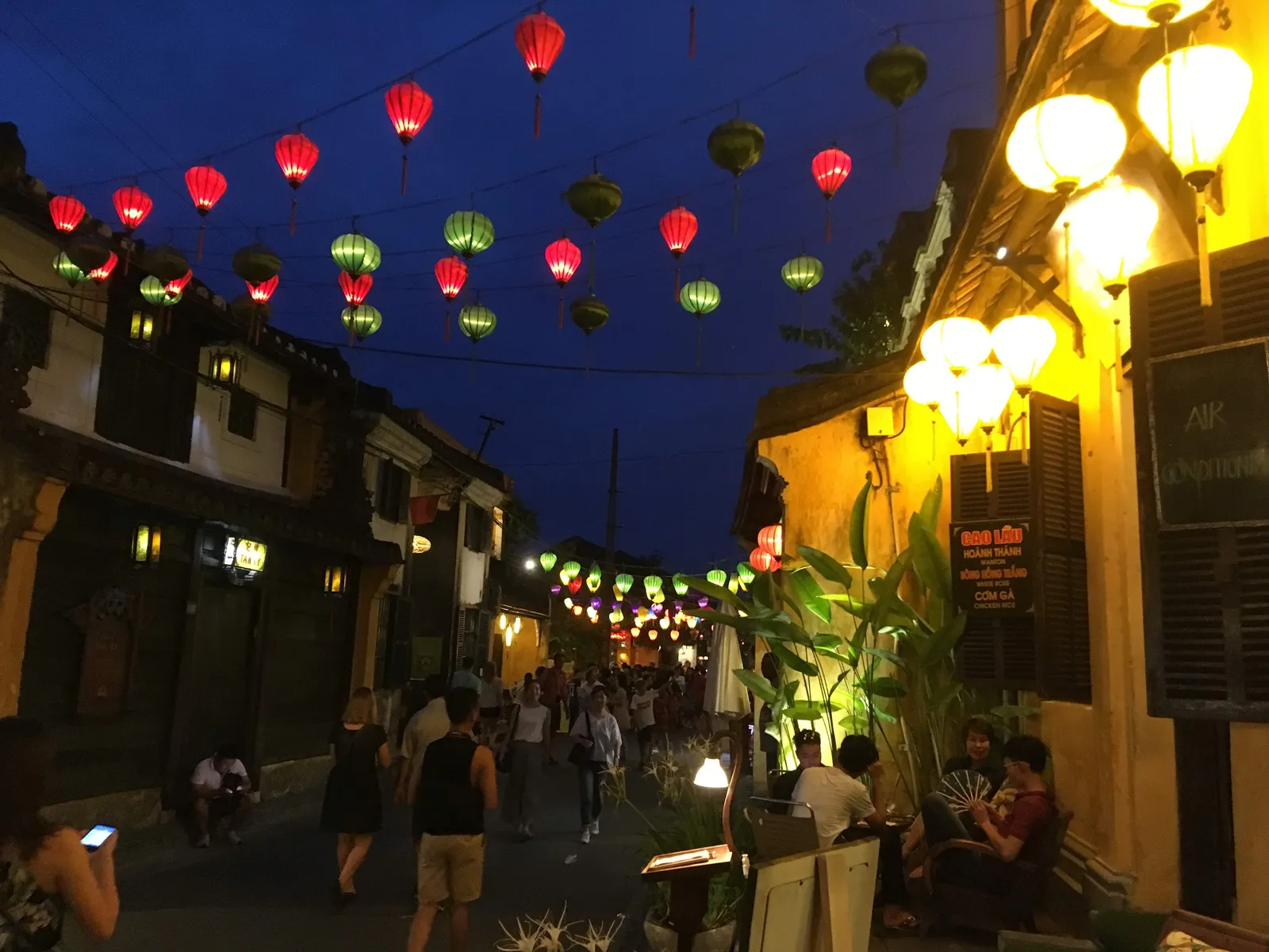 A Hội An old-town street at night, strung with red, green and yellow silk lanterns above walking crowds.