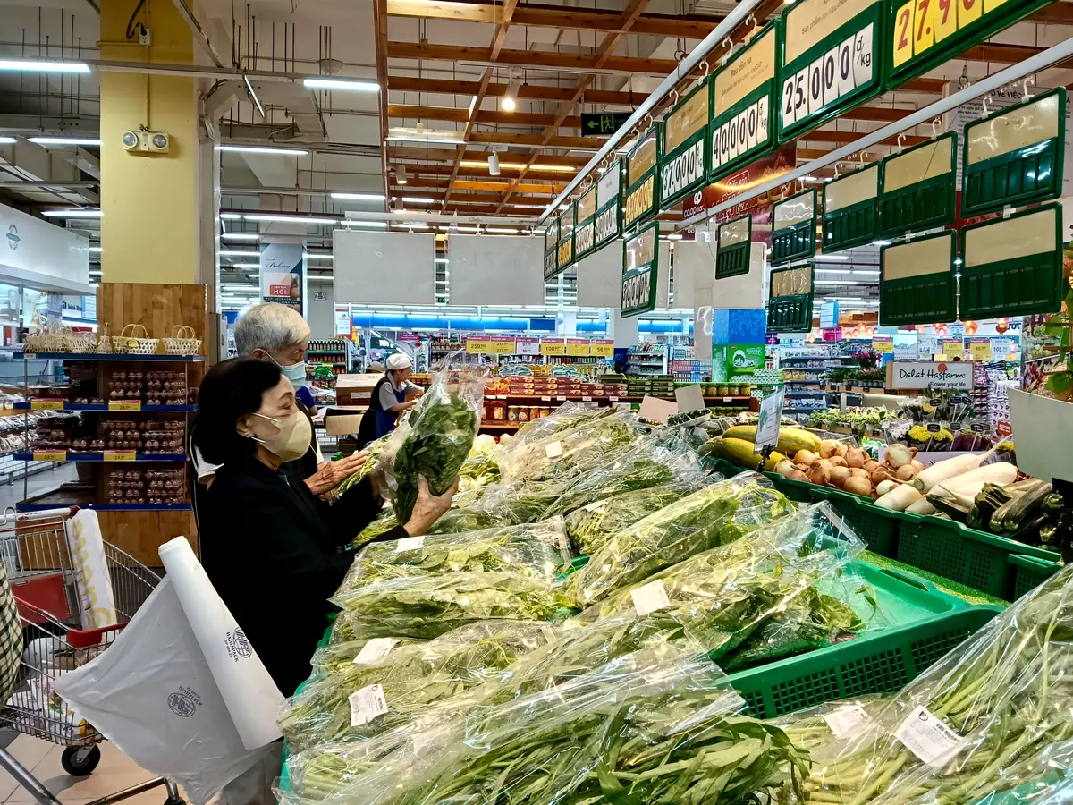 Wide supermarket aisle with fresh vegetables and signs hanging from the ceiling