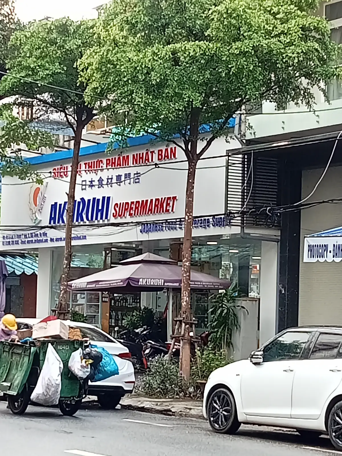 Street-front sign of a Japanese supermarket with an umbrella and trees outside