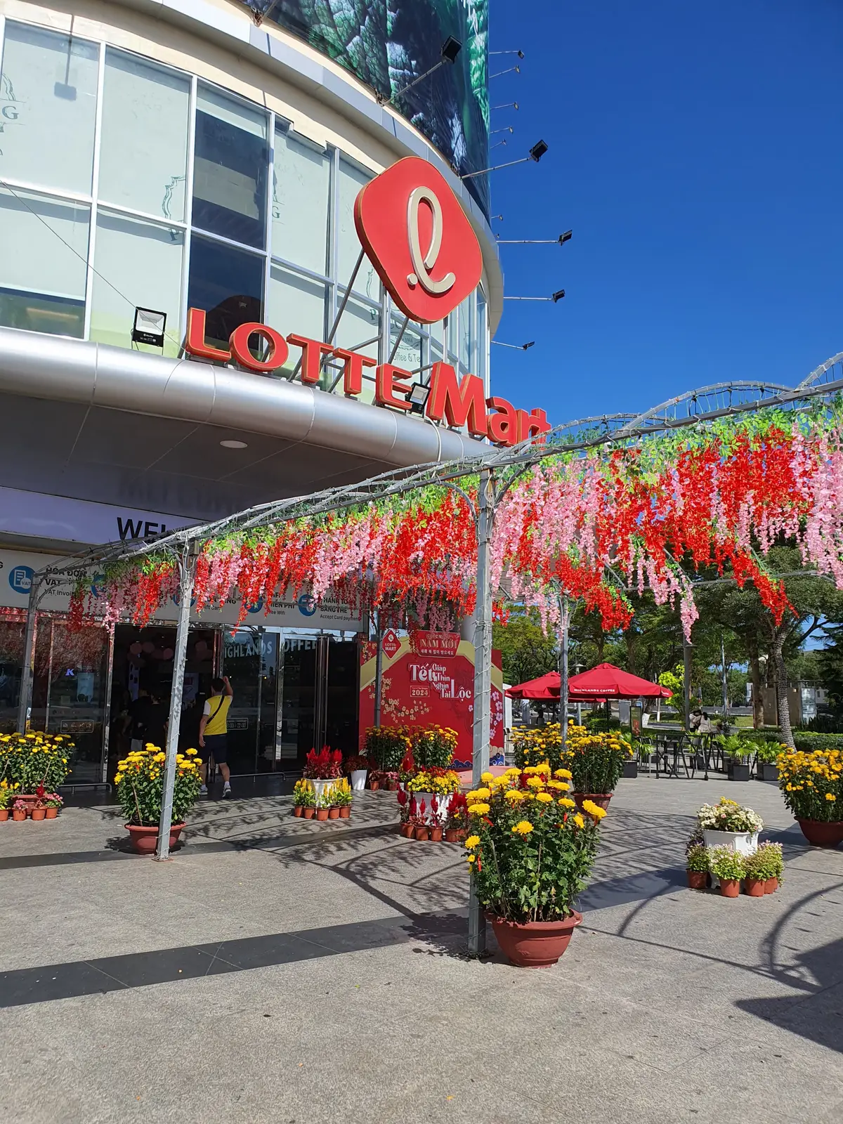 Entrance of a large supermarket with a red Lotte Mart sign and flower decorations overhead