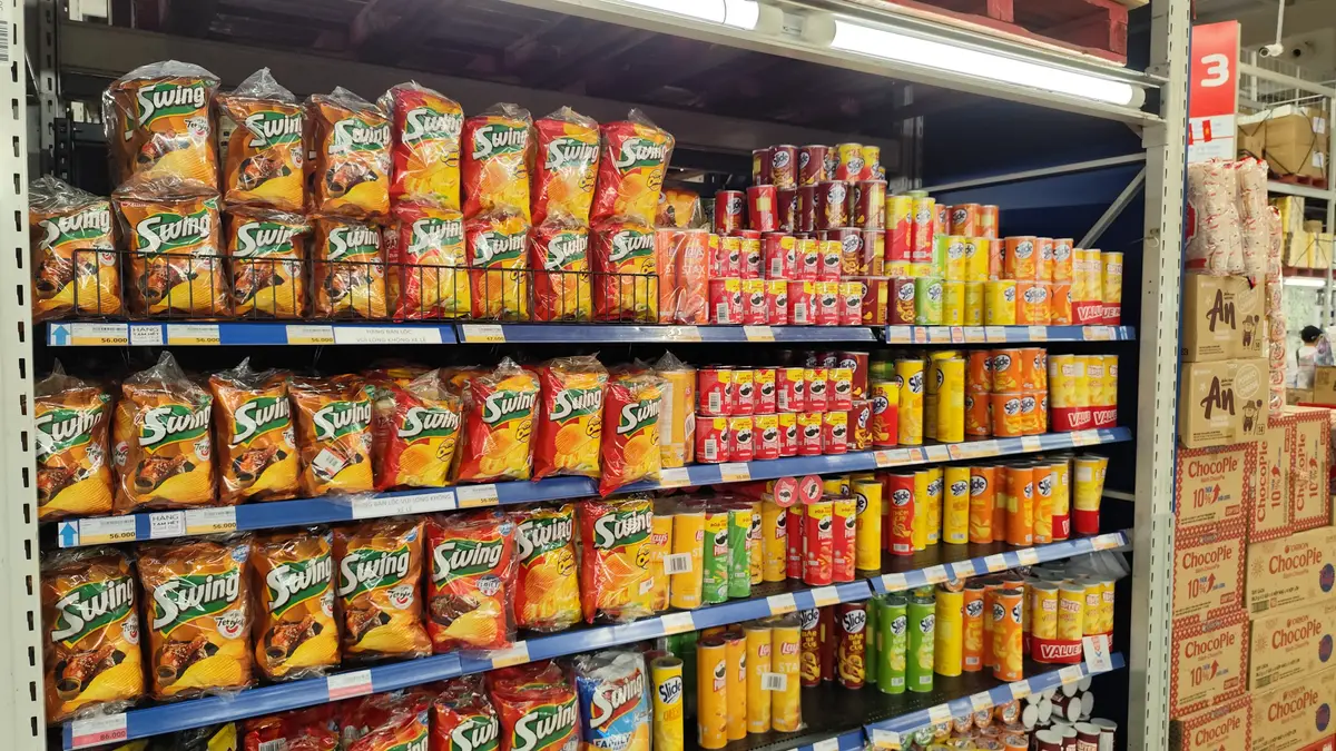Shelves of packaged snacks and drinks in a large supermarket aisle