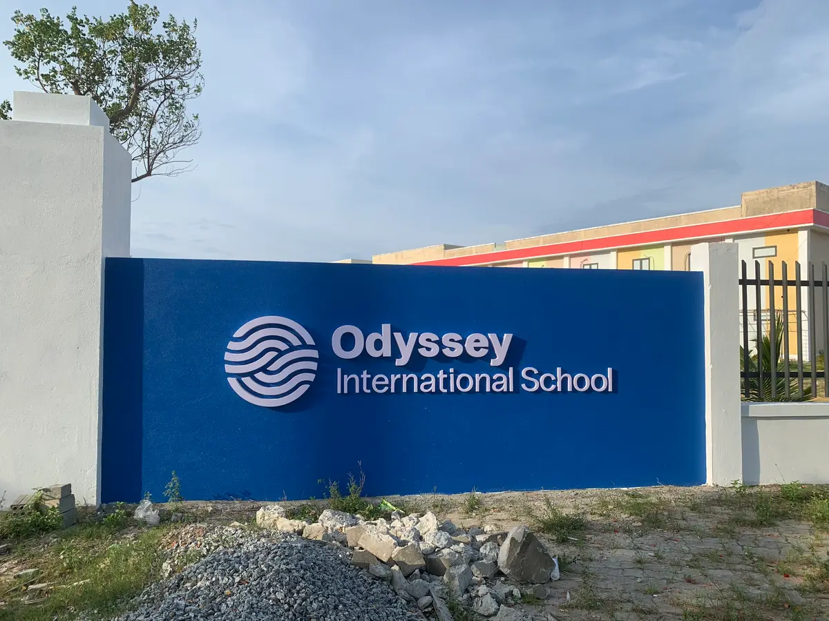 校园围栏旁的蓝色墙牌，写着Odyssey International School。