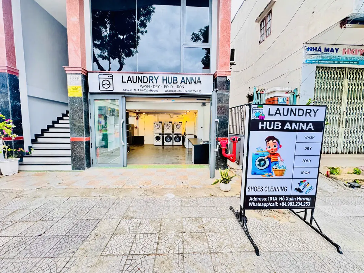 Laundromat front with washing machines visible through the glass door and a sandwich-board sign on the pavement