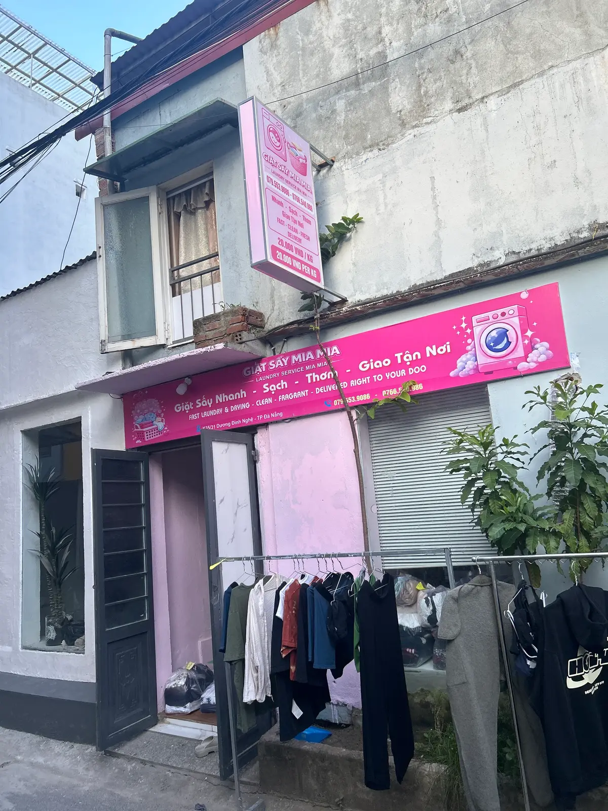 Street view of a narrow laundry shop with a bright pink sign and clothes hanging outside