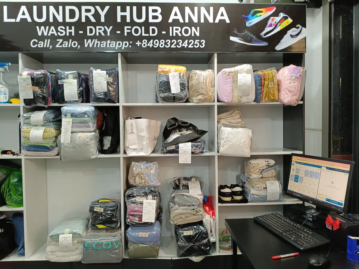 White shelving unit holding neatly bagged and folded laundry beside a computer at the counter