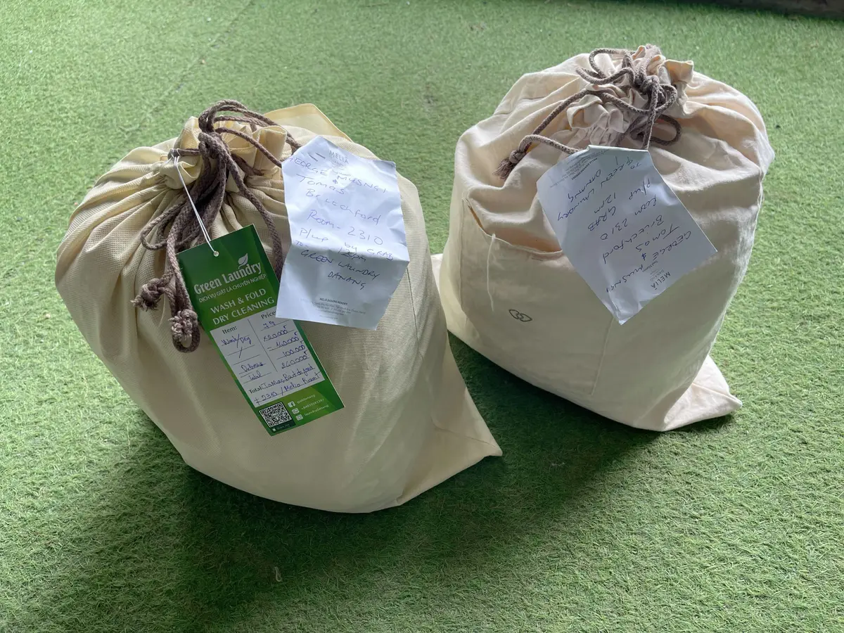 Two cloth laundry bags with tags sitting on green artificial grass