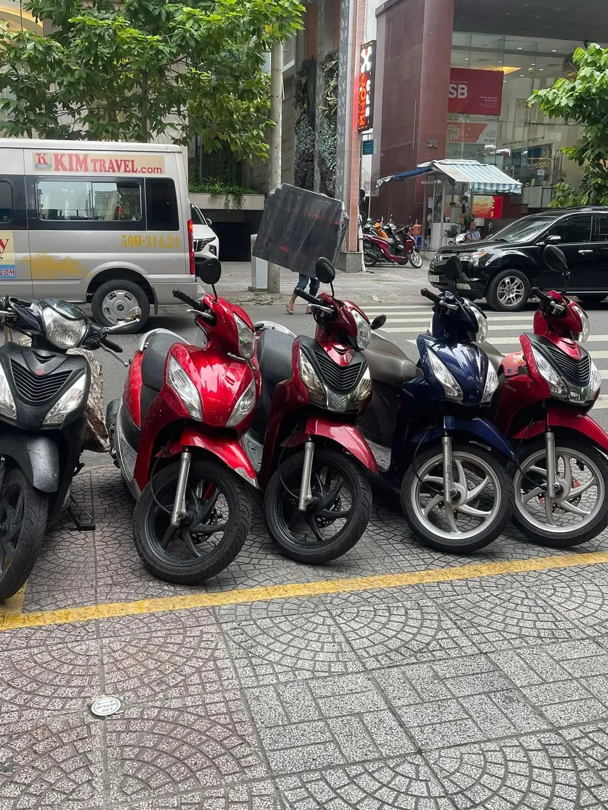 Vier rote und blaue Honda-Roller stehen entlang einer gelben Linie auf einem Gehweg in der Stadt.