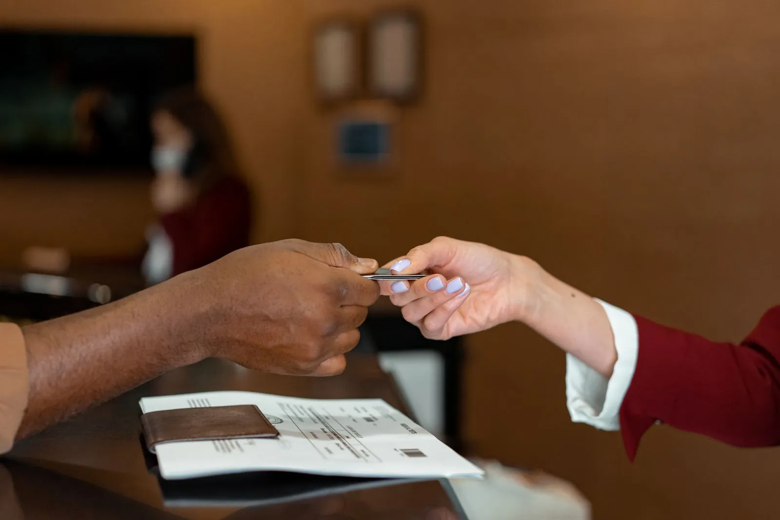A guest handing a card across a hotel reception counter, with a printed form and a passport wallet on the counter; the receptionist is out of focus