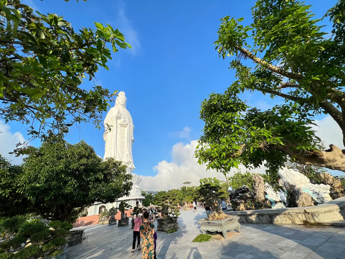 The tall white Lady Buddha statue rising above a courtyard with visitors and trees.
