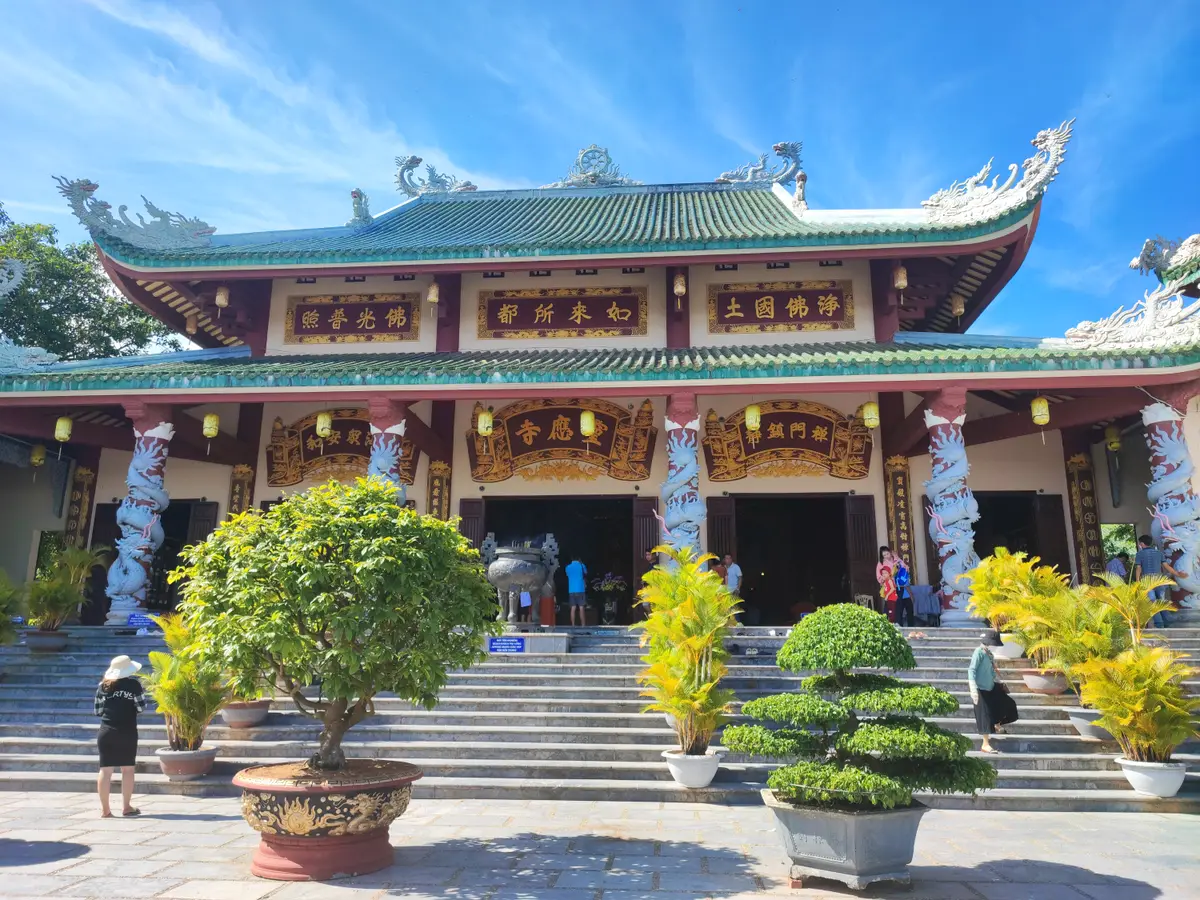 The pagoda's main hall with red columns and a curved, carved roof, potted plants lining the steps.