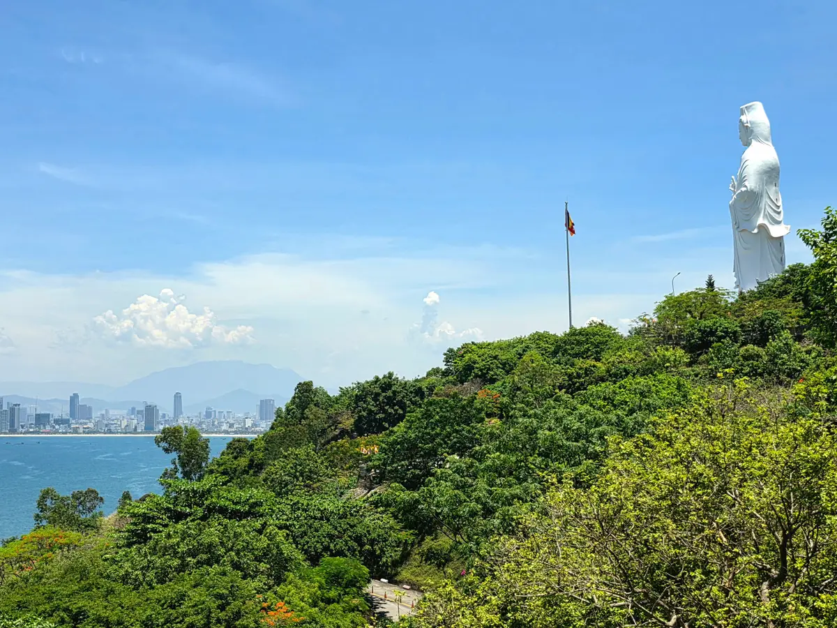 The white statue standing on a green hillside above the sea, the city coastline in the distance.