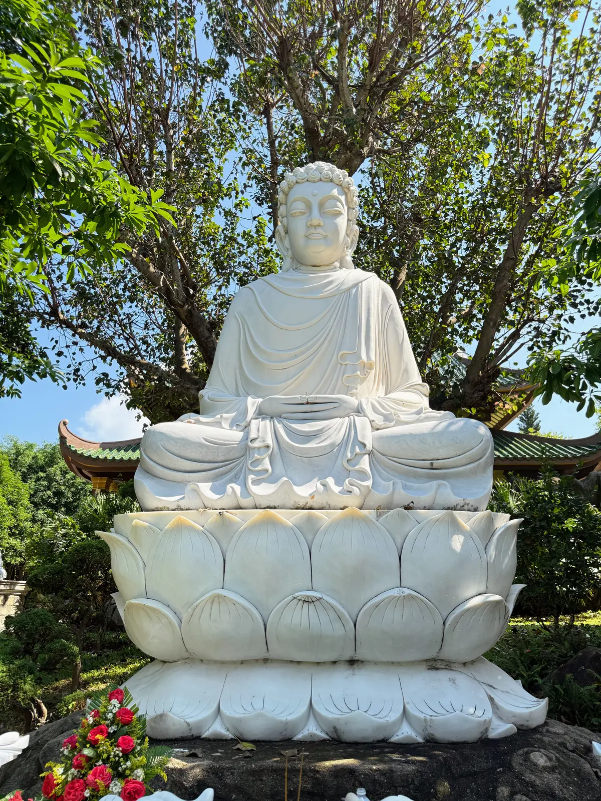 A white seated Buddha statue on a lotus pedestal under trees.