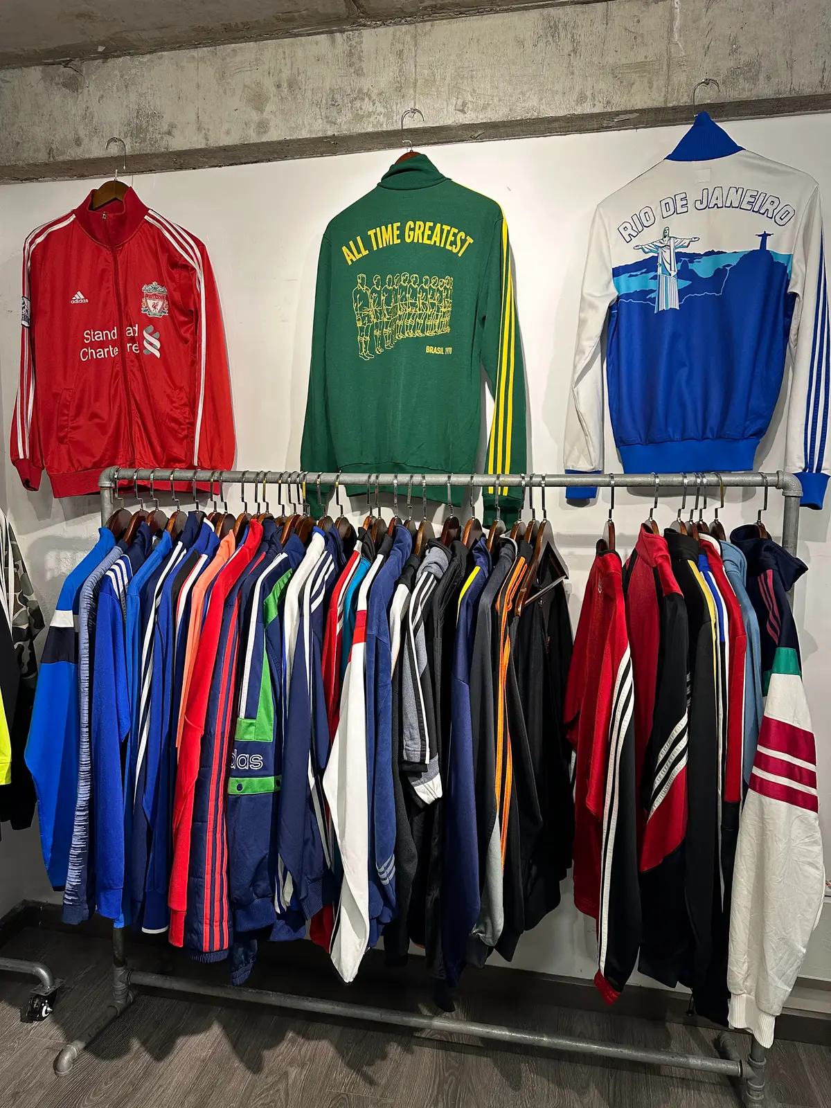 A rail of colourful second-hand track jackets under a row of sweatshirts on the wall.