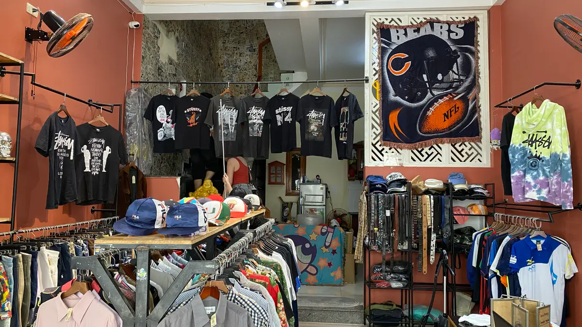 Band and graphic T-shirts hung on the wall of the Nighki2hand shop, with caps and rails of clothes below.