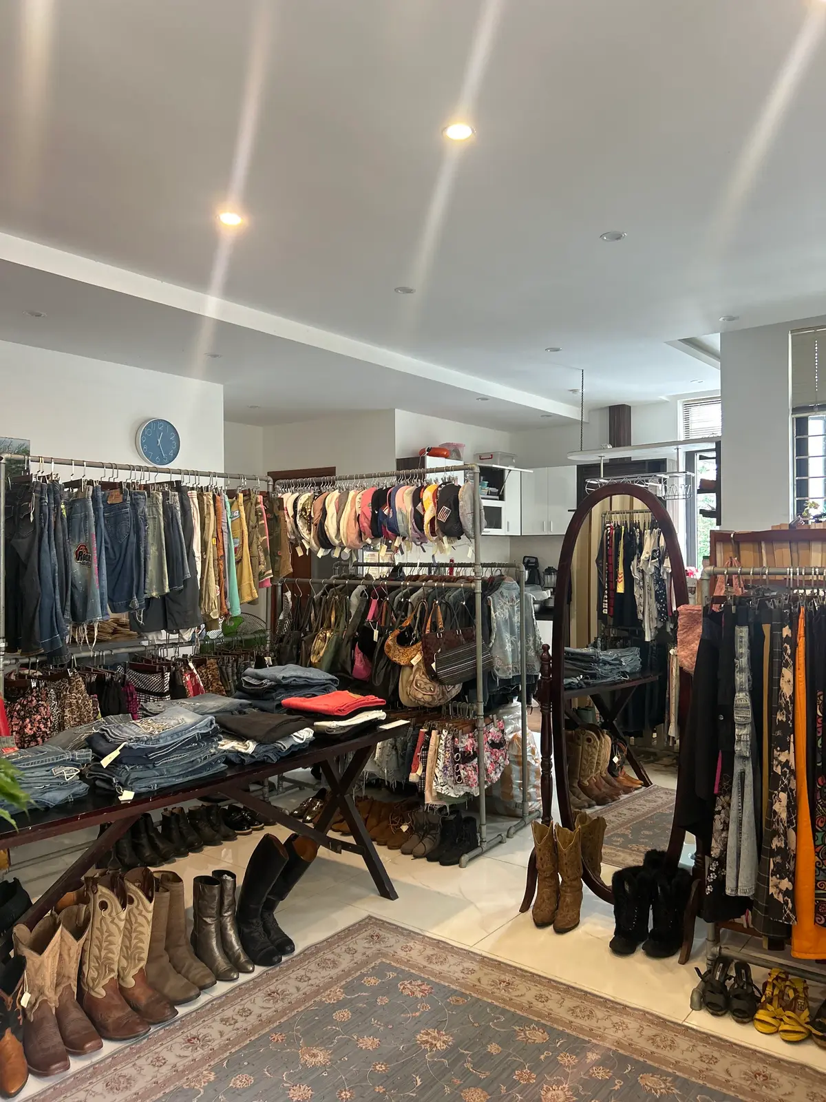 店内を広く見渡した様子:白いタイルの床に、ジーンズ、ジャケット、ドレスのラック、畳んだ服のテーブル、背の高い鏡がある。