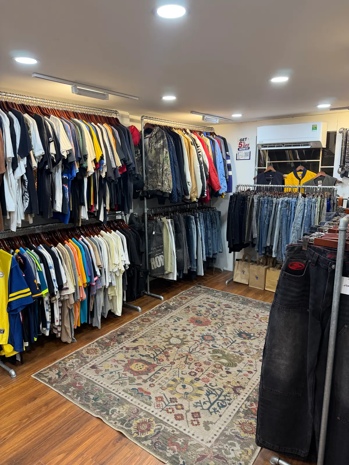 Rails of second-hand shirts, jackets and jeans on a patterned rug inside RMD Vintage Clothing Danang 2.