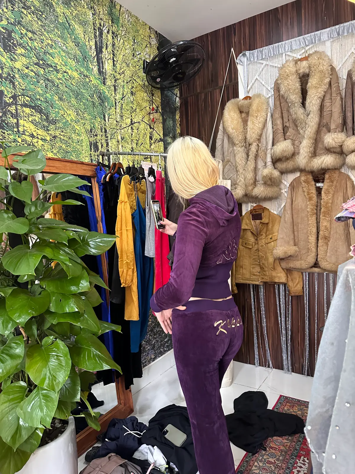 Inside the An Hai shop: a shopper browsing racks of coats, faux-fur jackets and dresses beside potted plants.