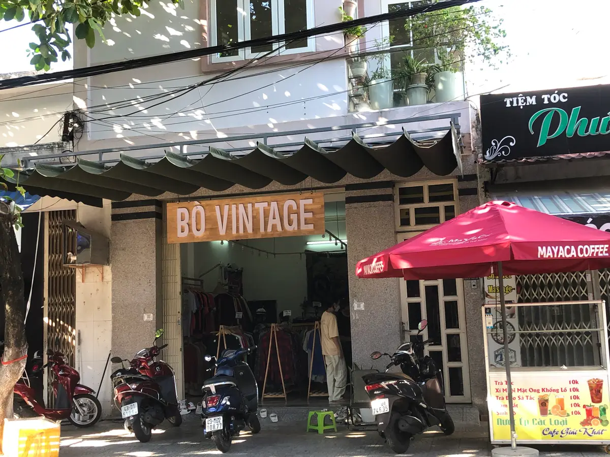 The narrow shopfront of Bo Vintage with its orange name sign, scooters parked in front and a red umbrella next door.