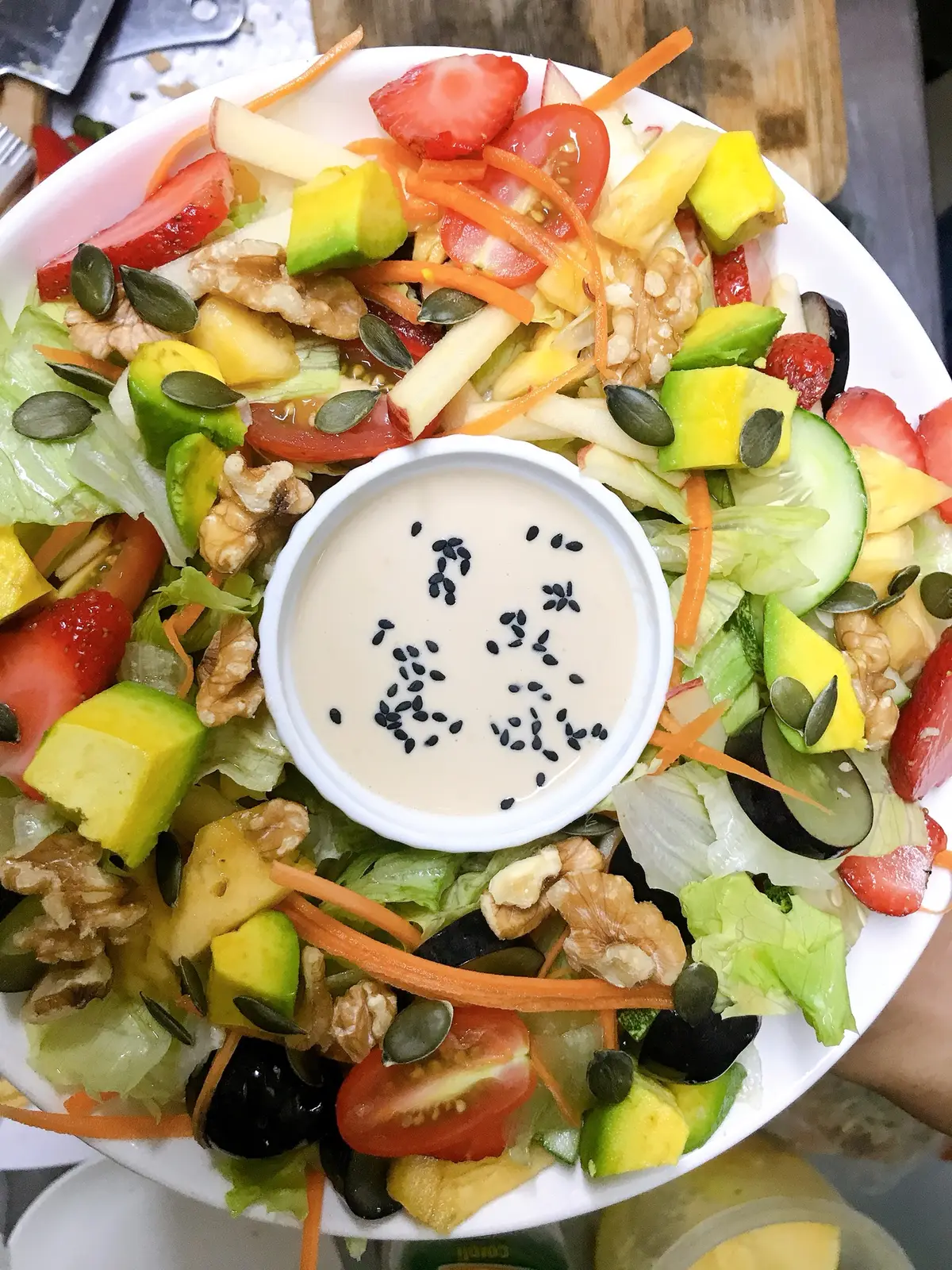 아보카도, 토마토, 오이, 호두를 올린 비건 샐러드와 작은 참깨 드레싱 그릇.
