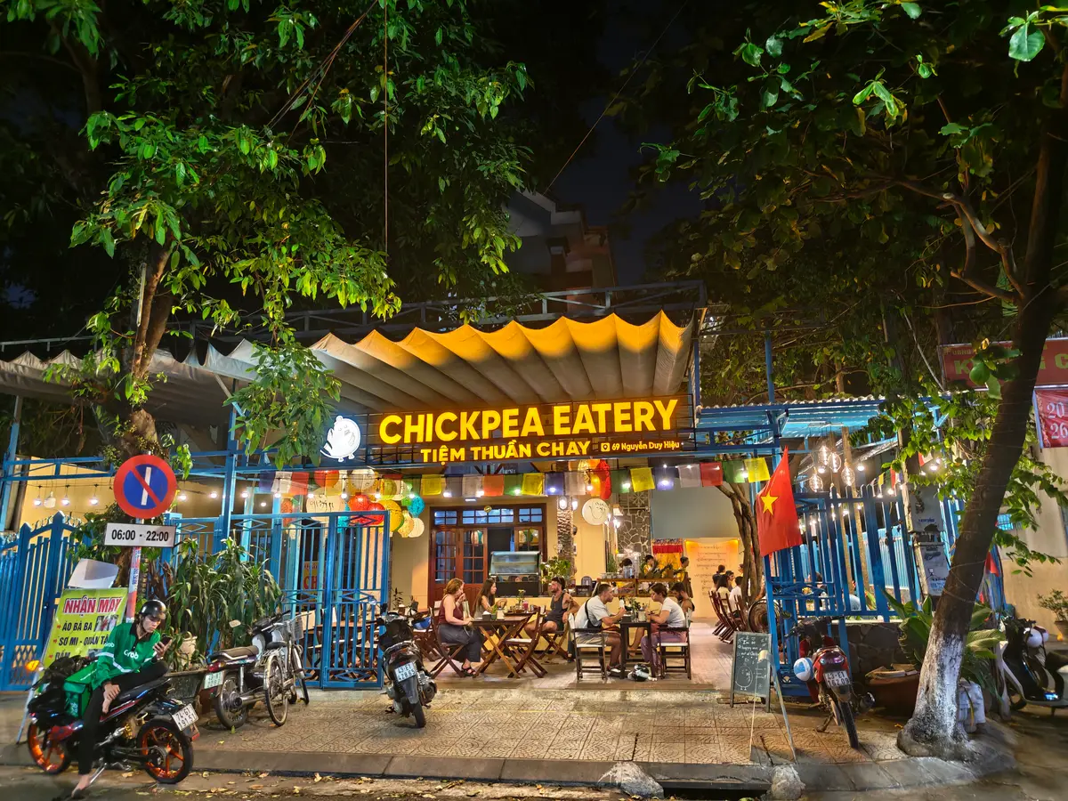 밤에 간판에 불이 들어온 Chickpea Eatery의 노란 가게 앞과 그 앞에 세워진 오토바이.