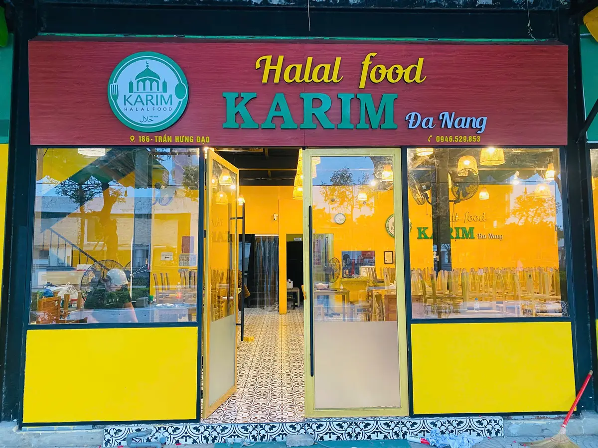 유리문과 노란 아래쪽 벽 위에 “Halal food KARIM Da Nang”이라고 적힌 빨간 간판이 달린 Halal Food Karim의 가게 앞.