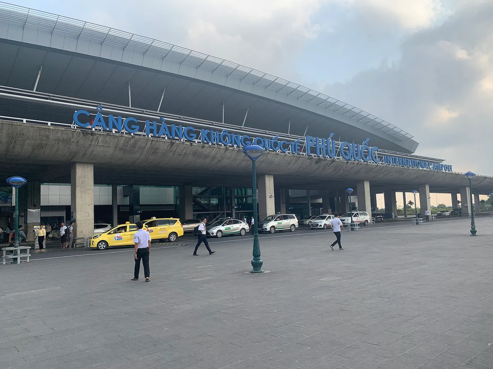 큰 파란색 간판 “Cảng hàng không quốc tế Phú Quốc / International Airport”가 달린 Phu Quoc 국제공항 정면과 밖에 주차된 택시