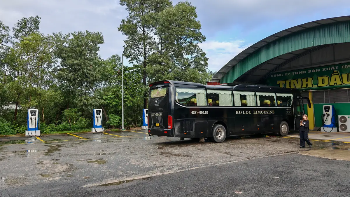 A black limousine bus parked in a car park near the border, with trees behind it.