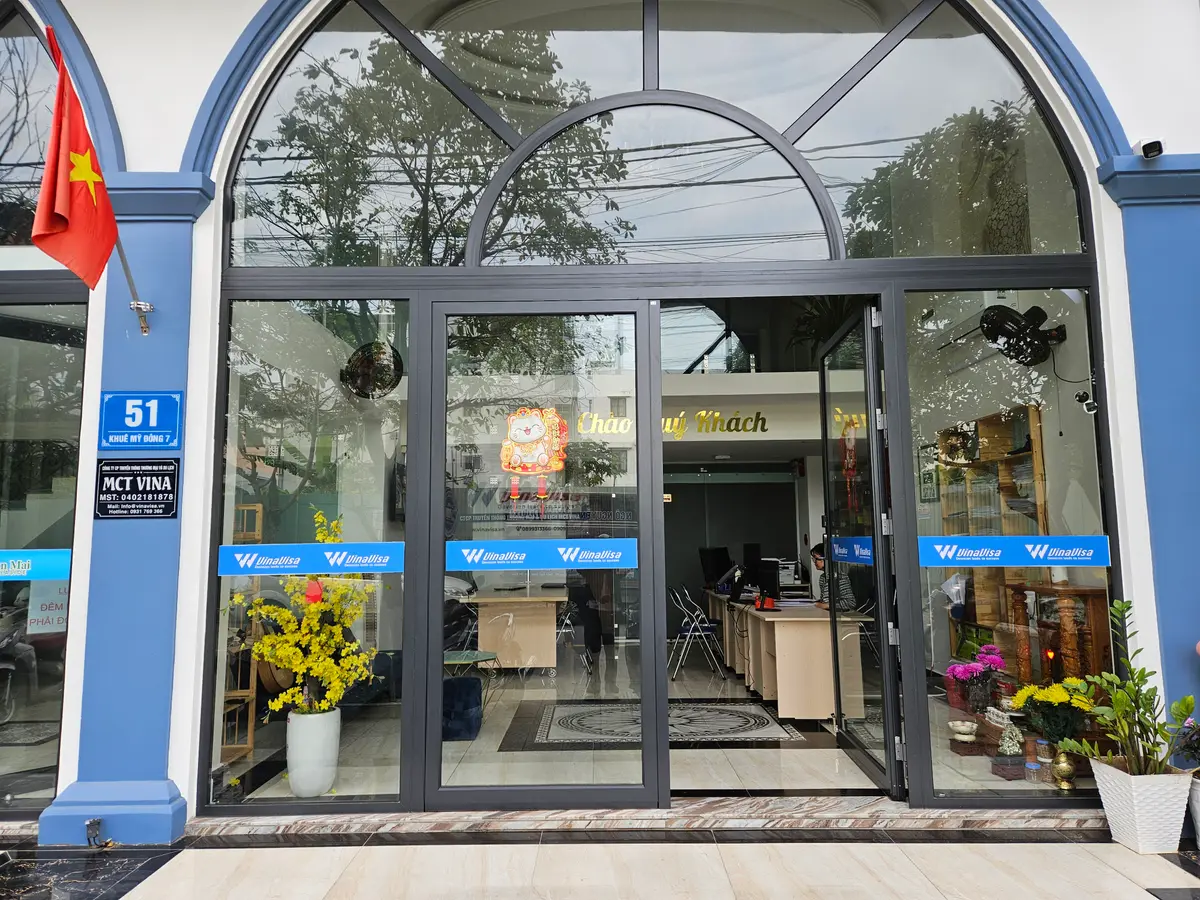 The arched glass shopfront of Vinavisa on Khue My Dong 7, with potted flowers by the doors.