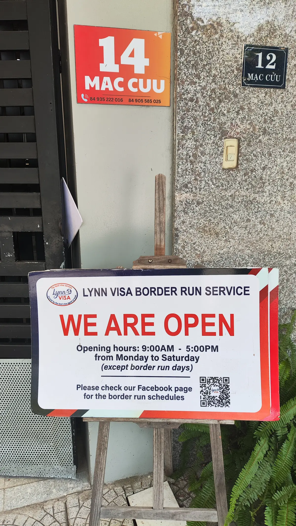 A Lynn Visa Border Run Service sign at the office door announcing that the office is open, with its opening hours.